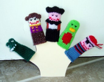 May include: Five finger puppets made of knitted yarn. The puppets are a green alligator, a brown and purple man with a hat, a green bird with red accents, a black and white man with a hat, and a blue, pink, and black man with a hat.