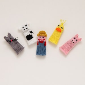 May include: Five knitted finger puppets, each with a different animal design. The puppets are gray, white, yellow, pink, and blue. The animals are a cat, a cow, a duck, a pig, and a farmer.