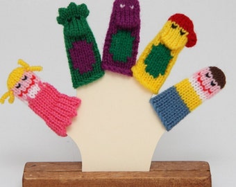 May include: Five colorful finger puppets on a wooden stand. The puppets are a girl with blonde hair, a boy with brown hair, a green and purple monster, a purple and green monster, and a yellow and green monster.