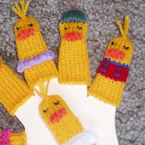 May include: Five knitted finger puppets shaped like yellow ducks with different colored accents. The puppets have embroidered eyes and beaks.