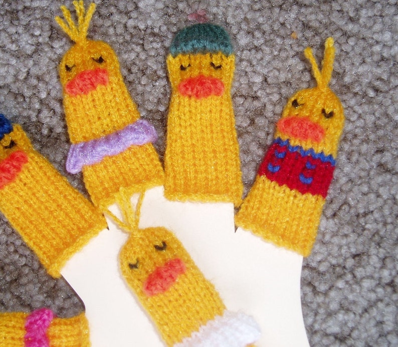 May include: Five knitted finger puppets shaped like yellow ducks with different colored accents. The puppets have embroidered eyes and beaks.