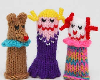 May include: Three knitted finger puppets. The first is brown with a blue collar, the second is purple with yellow hair and a pink face, and the third is white with red and pink accents and a colorful striped body.