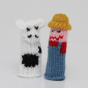 May include: Two knitted finger puppets, one a white cow with black spots and the other a blue and red farmer wearing a yellow hat.