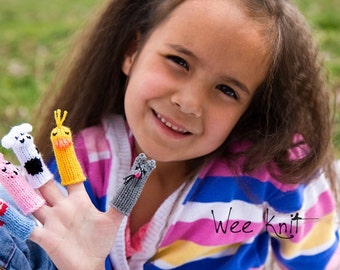 May include: A young girl wearing a pink and blue striped shirt with the text "Wee Knit" is wearing finger puppets on her fingers. The finger puppets are a cow, a chick, a pig, and a cat.