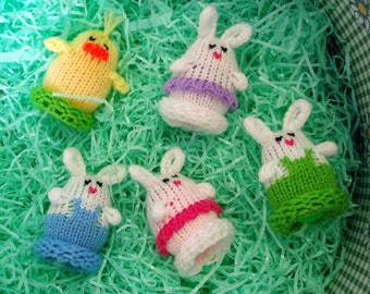 May include: Five knitted Easter egg ornaments, including a yellow chick and four bunnies. The bunnies are white with different colored accents, including purple, pink, green, and blue.