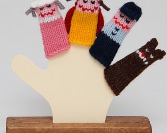 May include: A set of five finger puppets on a wooden stand. The puppets are made of knitted yarn in various colors, including pink, yellow, blue, brown, and red. The puppets have different facial expressions and features, such as a hat, a beard, and a nose.