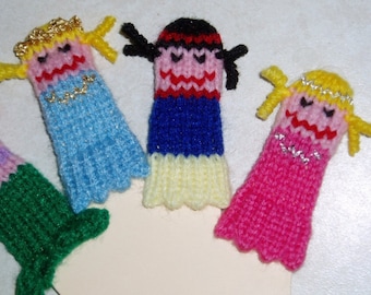 May include: Four finger puppets, each with a different color dress and hair. The puppets are made of knitted yarn and have embroidered faces. The puppets are arranged in a semi-circle on a white background.
