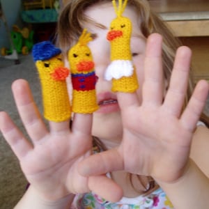 May include: A child's hand wearing three finger puppets. The puppets are yellow with red and blue details. The puppets are shaped like birds.