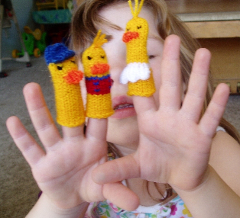 May include: A child's hand wearing three finger puppets. The puppets are yellow with red and blue details. The puppets are shaped like birds.