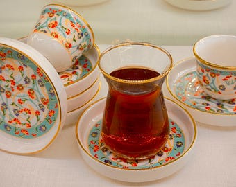 May include: A set of teacups and saucers with a floral pattern. The cups and saucers are white with a gold trim and feature a colorful floral design. A glass of tea is also included in the image.