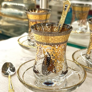 Peut inclure: Ensemble de tasses à thé en verre ornées de filigranes dorés et de soucoupes assorties. Chaque tasse a un bord doré et est accompagnée d'une cuillère décorative. L'ensemble est conçu pour servir le thé.