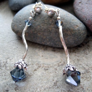 May include: Silver dangle earrings with a dark blue crystal at the bottom and a silver flower design above the crystal.