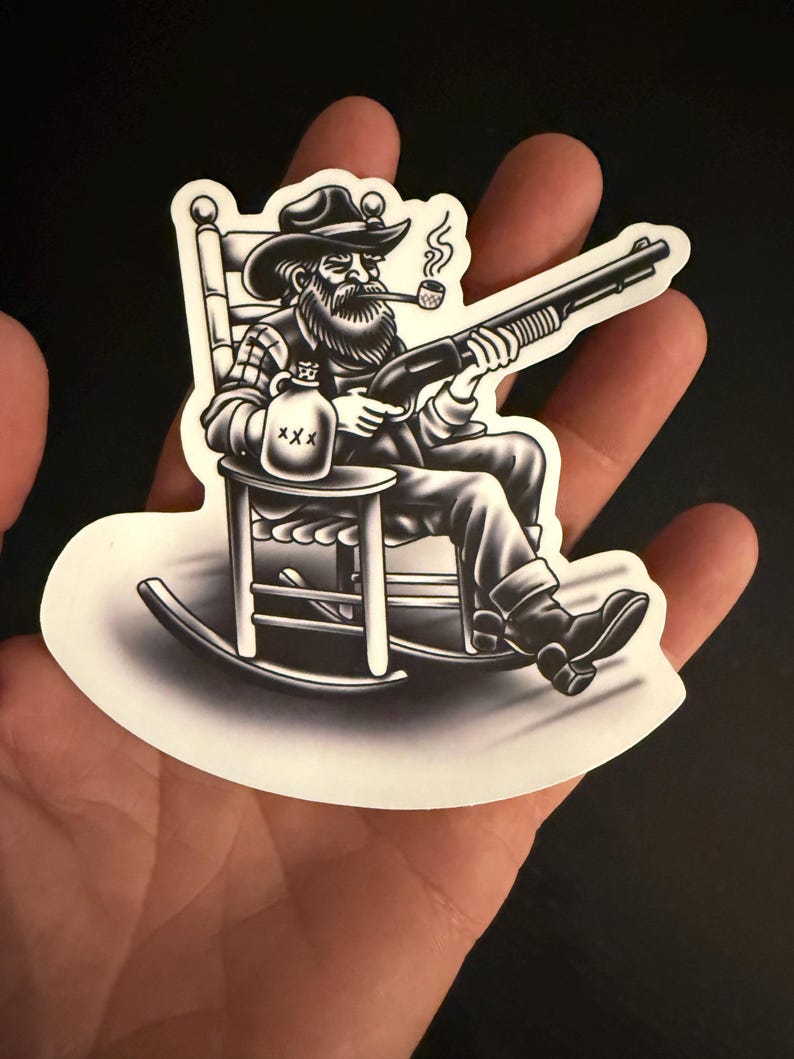 Puede incluir: Adhesivo en blanco y negro que representa a un hombre barbudo con sombrero de vaquero, fumando en pipa y sosteniendo una escopeta, sentado en una mecedora. Una botella marcada con "XXX" est&aacute; a su lado. Borde blanco.