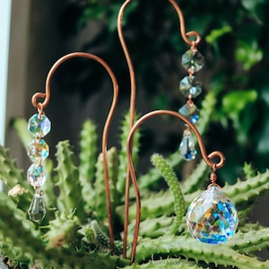 May include: Three copper wire garden stakes with crystal prisms hanging from them. The stakes are inserted into a pot of green succulents.
