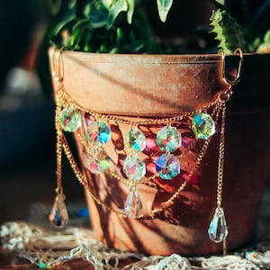 May include: A gold chain necklace with iridescent crystal beads and teardrop pendants. The necklace is draped over a terracotta flower pot.