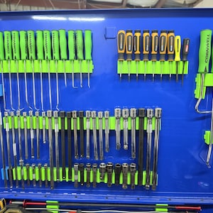 May include: A blue metal tool storage cabinet lid interior featuring organized rows of green-handled Cornwell screwdrivers, GearWrench screwdrivers, and various chrome socket extensions and adapters held in place by bright green plastic racks.