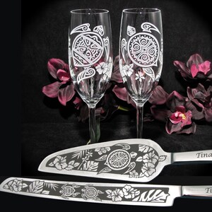 May include: A set of two champagne flutes and a cake server with an etched design of a turtle and hibiscus flowers. The glasses and server are made of clear glass and have a silver finish.