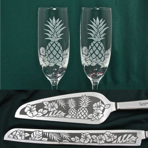 May include: Two etched champagne flutes with pineapple designs and a matching cake server with pineapple and hibiscus flower designs.