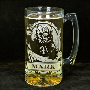 May include: A clear glass beer stein with a handle. The stein is etched with a black bear design and the name "MARK".