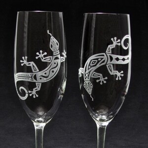May include: Two clear glass champagne flutes with etched designs of stylized lizards. The lizards are in a black and white pattern.