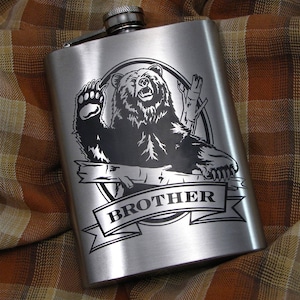May include: A silver flask with a black bear graphic and the word "BROTHER" engraved on a banner. The bear is standing on its hind legs with its paws raised.
