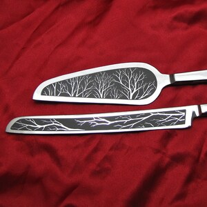 May include: A set of two silver cake knives with black handles. The blades are engraved with a design of trees.