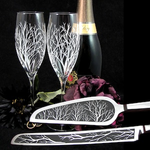May include: A wedding cake cutting set featuring a black and white tree design. The set includes a knife and a server. Both the knife and server are made of metal with black handles. The tree design is etched into the metal.