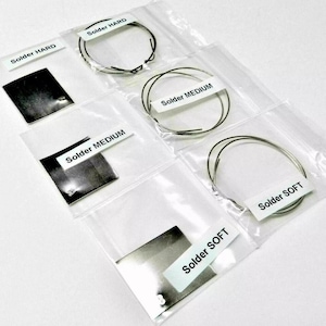 May include: Four clear plastic bags each containing a small silver square and a roll of silver solder wire. The bags are labeled "Solder HARD", "Solder MEDIUM", "Solder MEDIUM", and "Solder SOFT".