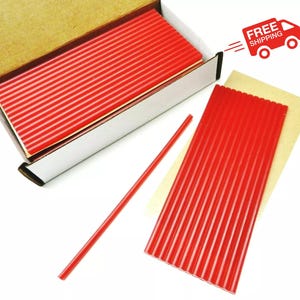 May include: A box of red wax sticks, with some sticks laid out on a brown surface. The box is open and the wax sticks are visible inside. The wax sticks are about 1/4 inch in diameter and are about 6 inches long.