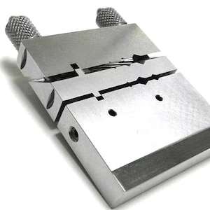 May include: A silver metal tool with two adjustable knobs. The tool has a slot in the center for holding a small object.