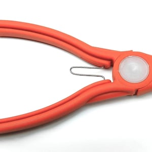 Peut inclure: Pince orange avec un centre blanc et un ressort argenté. L'outil a une poignée incurvée et une tête arrondie. La pince est conçue pour une tâche spécifique, probablement dans la fabrication de bijoux ou l'artisanat.