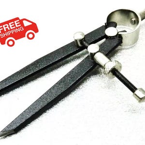 May include: A black metal compass with a silver adjustment knob and a silver ring. The compass has a pointed tip on one end and a small, round knob on the other end.