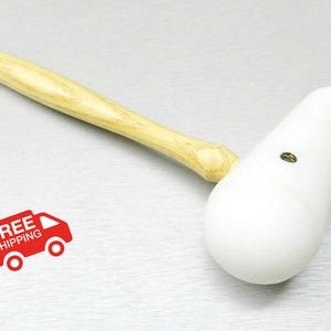 Puede incluir: Un mazo blanco con un mango de madera de color claro. La cabeza del mazo tiene forma de pera. El mango es de color marrón claro. La imagen también incluye un gráfico rojo con las palabras "FREE SHIPPING" y un camión.