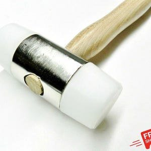 May include: A white rubber mallet with a silver metal band and a light-coloured wooden handle. The mallet is designed for general use. The handle is approximately 20 cm long.
