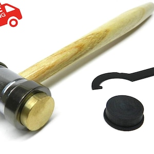 May include: A metal and wood mallet with a brass striking face, a black wrench, and a black rubber cap. The mallet has a light-coloured wooden handle. The image includes a red delivery truck icon.