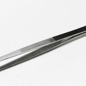 Puede incluir: Pinzas de acero inoxidable con una banda negra y un mango plateado. Las pinzas tienen un área de agarre estriada y puntas afiladas. La herramienta está diseñada para trabajos de precisión.