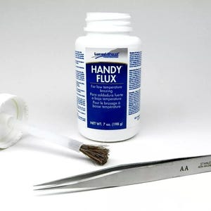 Może przedstawiać: Biała butelka topnika do lutowania Lucas Milhaupt Handy Flux z niebieską etykietą. Etykieta zawiera napis "Handy Flux" i "Do lutowania w niskiej temperaturze". Butelka ma pojemność 7 uncji (198 gramów).
