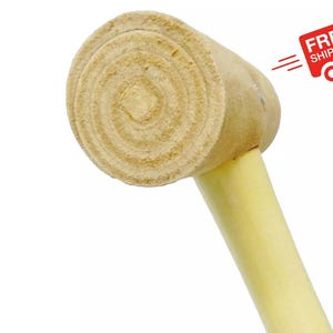May include: A wooden mallet featuring a cylindrical head with a visible natural wood grain pattern and a smooth, light-colored handle. The head displays concentric circular textures on its flat striking surface, showcasing the raw, unfinished wood material.