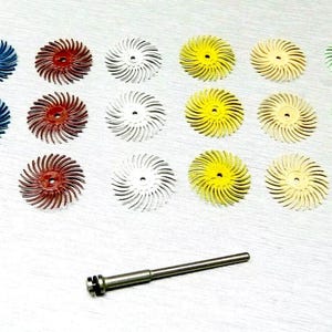 以下が含まれることがあります： 青、赤、白、黄、緑など、さまざまな色の研磨ホイール18個セット。ホイールは銀色の表面にグリッドパターンで配置されています。金属シャフトも含まれています。