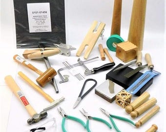 May include: A jewellery making kit with a variety of tools, including a hammer, pliers, a saw, a mandrel, and a sanding block. The kit also includes a pair of safety glasses and a sheet of sandpaper. The kit is packaged in a clear plastic bag with a label that reads "Assortment Pack 8 pc Jewellery Making Kit 81127 13"