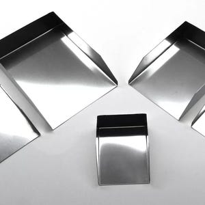 May include: Set of five stainless steel scoops in various sizes. The scoops are angled and have a smooth, shiny finish.