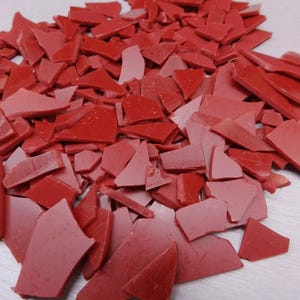 May include: A pile of red wax flakes. The wax is broken into irregular shapes and sizes.