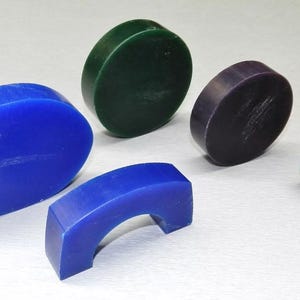 Puede incluir: Surtido de cinco bloques de cera de diferentes colores para la elaboración de joyas. Los bloques son de diversas formas, incluyendo redonda, ovalada y una forma curva con un agujero en el centro. Los colores son azul, verde y morado.