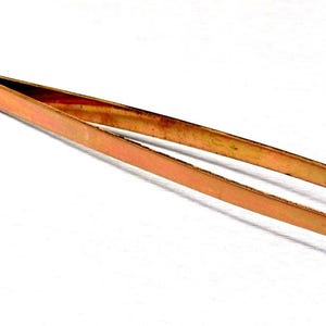 May include: A pair of copper-coloured tweezers, angled and curved at the tips. The tweezers have a flat, rectangular handle with two small rivets. The tool is designed for precision work and is set against a white background.