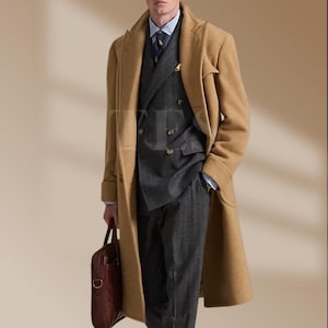 May include: A tan overcoat with a double-breasted gray suit, blue shirt, and patterned tie. The suit has pinstripes. A brown leather briefcase is held in the left hand. The coat has a classic, tailored design.