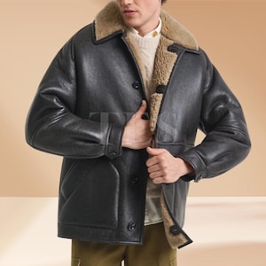Könnte beinhalten: Schwarze Lederjacke mit Schafsfellkragen und -futter. Die Jacke hat eine Knopfleiste vorne und ein klassisches Design. Das Schafsfell ist hellbraun.