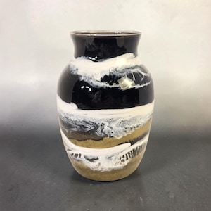 May include: A decorative vase with a glossy finish. The vase features a black top, white and black swirling middle section, and a tan and white base. The vase has a rounded shape and a narrow neck. The vase is suitable for home decor.