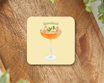 May include: A yellow coaster with a cartoon illustration of a cocktail with two yellow ducklings and a green leaf on top. The text "Quacktail" is written above the cocktail.