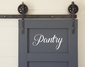 May include: A gray sliding door with a white vinyl sticker that says "Pantry" on it. The door has a black metal track and two black metal rollers.