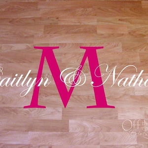 May include: A pink "M" initial with the names Caitlyn & Nathan in white cursive script on a wood floor. The text "Off the Wall Expressions" is in the bottom right corner.